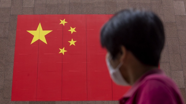 A pedestrian wearing a protective mask walks past a Chinese national flag displayed outside a hotel on National Day in Hong Kong, China, on Thursday, Oct. 1, 2020.