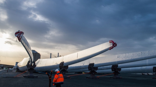 A worker passes wind turbine blades at the Siemens Gamesa Renewable Energy SA plant at the Port of Le Havre in Le Havre, France, on Monday, April 11, 2022. French government coffers are getting a boost from renewable energy as record power prices reduce state subsidies and even trigger reimbursements from the industry, the country’s wind trade group said.