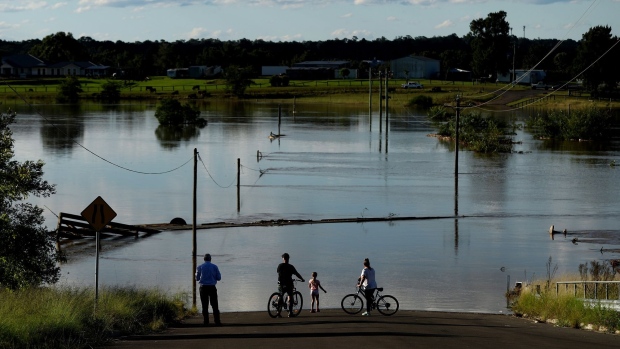 People look out at floodwaters from a closed road in the suburb of Pitt Town Bottoms in Sydney, Australia, on Wednesday, March 24, 2021. The one-in-100 year flooding event in recent days is causing supply disruptions in Australia. Photographer: Brent Lewin/Bloomberg