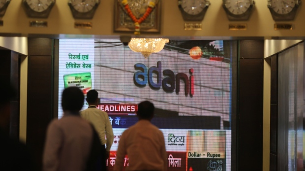 People walk past a screen displaying news featuring on Adani Group inside the BSE building in Mumbai, India, on Thursday, Feb. 2, 2023. Adani’s businesses have lost $107 billion in a week, one of the biggest wipeouts in India’s history, after an explosive report by short-seller Hindenburg Research forced him to pull a stock sale at the 11th hour and led some lenders to reject his securities as collateral for client trades. Photographer: Dhiraj Singh/Bloomberg