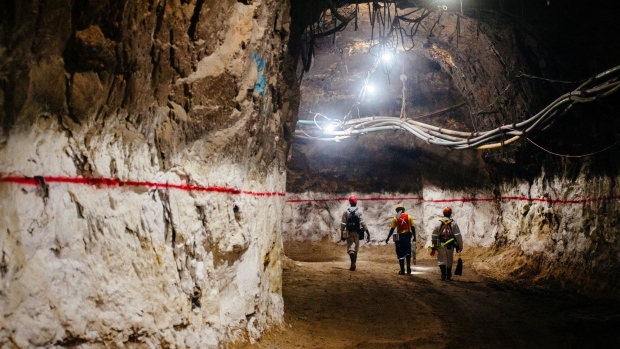 Miners walk through an underground tunnel illuminated with lights at the South Deep gold mine, operated by Gold Fields Ltd., in Westonaria, South Africa, on Thursday, March 9, 2017. South Deep is the world's largest gold deposit after Grasberg in Indonesia, makes up 60 percent of the company's reserves and the miner says it's capable of producing for 70 years. Photographer: Waldo Swiegers/Bloomberg