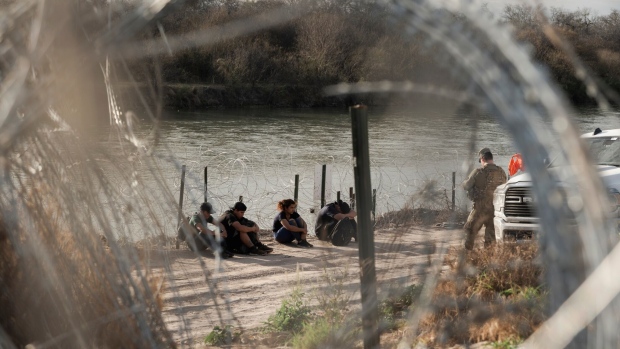 <p>Migrants wait with members of the Texas National Guard to be processed by border patrol along the banks of the Rio Grande River in Eagle Pass, Texas, on Feb. 23.</p>