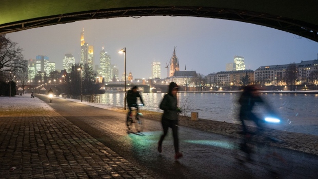 A jogger and cyclists pass along a towpath as skyscrapers stand illuminated on the skyline beyond the River Main in Frankfurt, Germany, on Thursday, Jan. 24, 2019. ECB President Mario Draghi intensified his warning on the challenges facing the euro-area economy, signaling the European Central Bank could be even more cautious about any withdrawal of crisis-era stimulus this year. Photographer: Jasper Juinen/Bloomberg